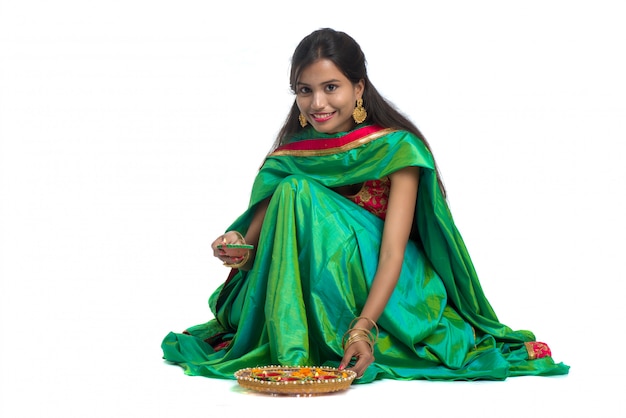 Ritratto di una ragazza tradizionale indiana che tiene Diya e che produce Rangoli. Ragazza che celebra Diwali o Deepavali con la lampada a olio della tenuta durante il festival di luce su fondo bianco