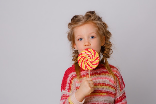 Ritratto di una ragazza una bambina bionda con una lecca-lecca su un bastone sorridente in abiti colorati