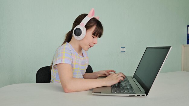 Ritratto di una ragazzina con le cuffie wireless che usa un portatile e studia online a casa