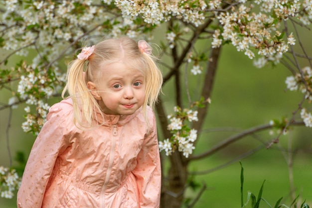 Ritratto di una ragazzina sorpresa o frustrata fuori vicino a un albero in fiore con una grimace divertente sul suo viso il giorno di primavera