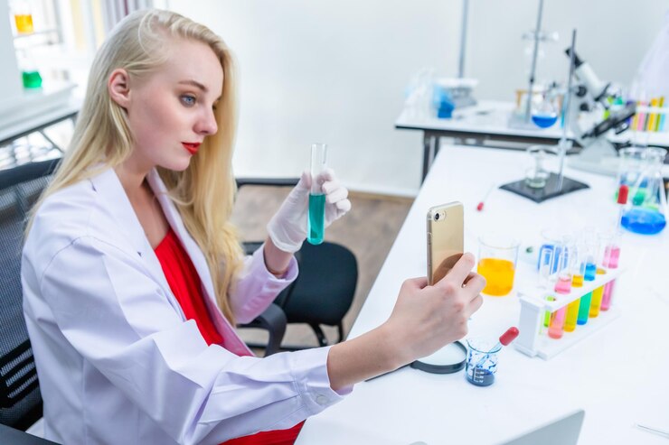 Foto ritratto di una ricercatrice che effettua ricerche in uno scienziato di laboratorio di chimica che tiene una provetta con un campione che prende un selfie con focus sullo smartphone in background di analisi di laboratorio