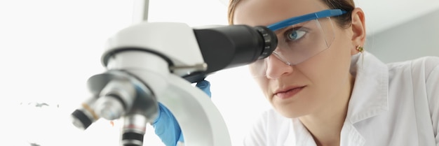 Ritratto di una scienziata che guarda attraverso il microscopio in laboratorio sta facendo una giovane scienziata