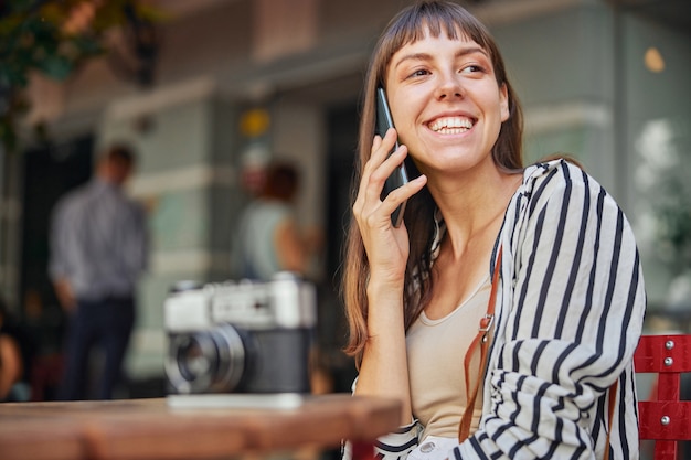 Ritratto di una signora sorridente che parla al telefono mentre è seduto fuori dal caffè