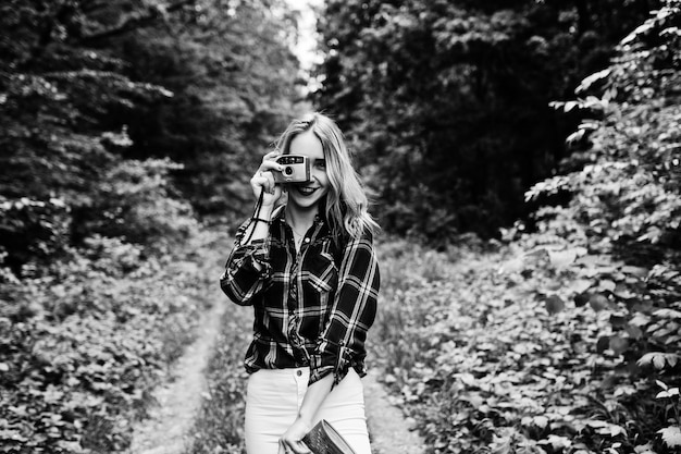 Ritratto di una splendida ragazza in camicia scozzese che scatta foto con la fotocamera nella foresta