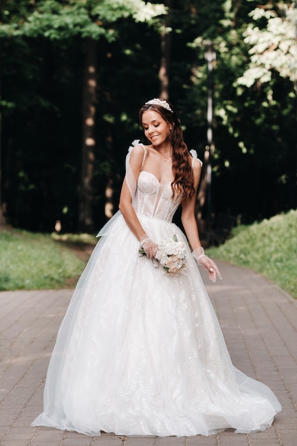 Ritratto di una sposa elegante in un abito bianco con un bouquet in natura in un parco naturale. Modello in abito da sposa e guanti e con un bouquet .Bielorussia