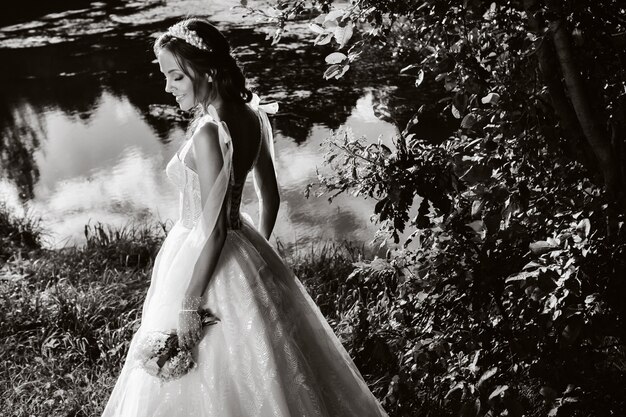 Ritratto di una sposa elegante in un abito bianco con un bouquet in natura in un parco naturale. Modello in abito da sposa e guanti e con un bouquet .Bielorussia