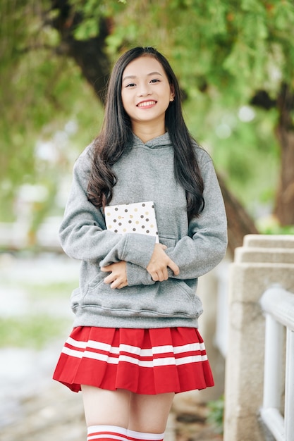 Ritratto di una studentessa asiatica sorridente felice che tiene un diario o un diario e quando si trova in un parco