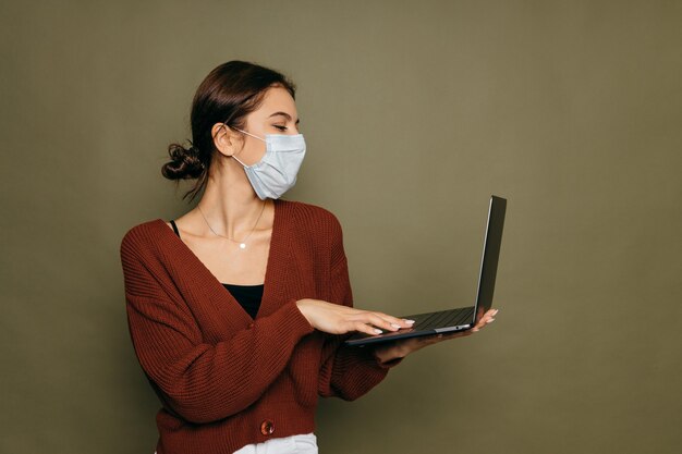 Ritratto di una studentessa in una maschera protettiva con un laptop su uno sfondo verde. Foto di alta qualità