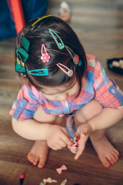 Ritratto di una testa di bambina carina con molti fermagli per capelli che giocano su un pavimento di legno a casa. Messa a fuoco selettiva sulla testa.