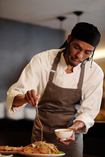 Ritratto di uno chef che versa un condimento piccante su un'insalata di verdure fresche