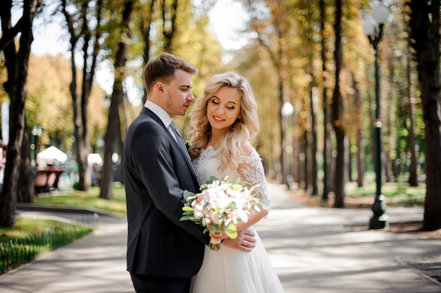 Ritratto di uno sposo che abbraccia una sposa bionda nel parco