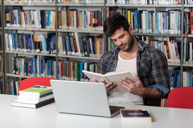 Ritratto di uno studente attraente che fa un po' di lavoro scolastico con un computer portatile in biblioteca