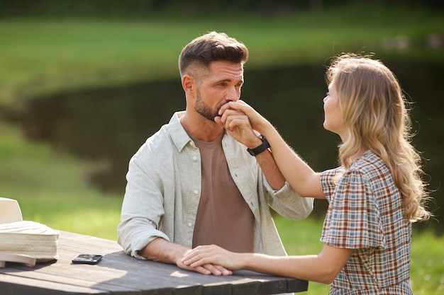 Ritratto di uomo adulto bello che bacia la mano di bella donna mentre vi godete un appuntamento romantico all'aperto in riva al lago