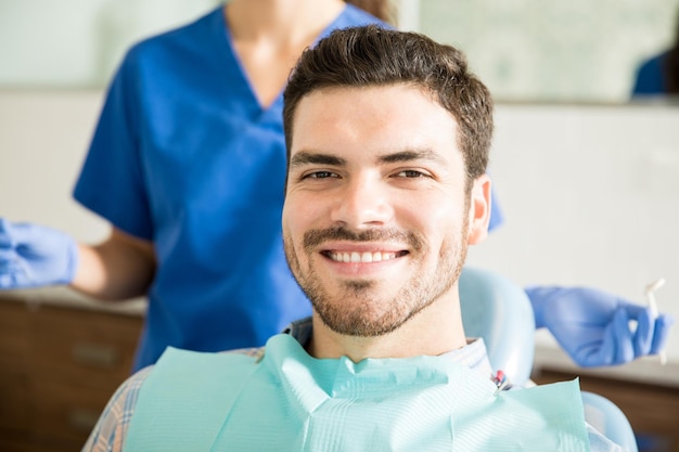 Ritratto di uomo adulto metà sorridente con il dentista che tiene strumenti dentali in clinica