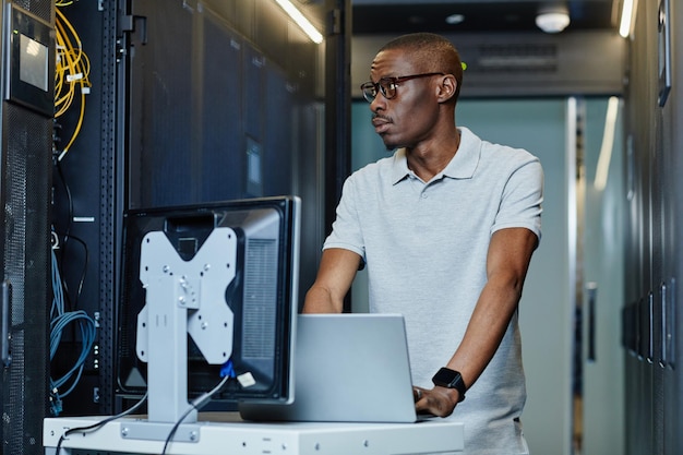 Ritratto di uomo afroamericano che collega il laptop al server nella sala server e configura Internet