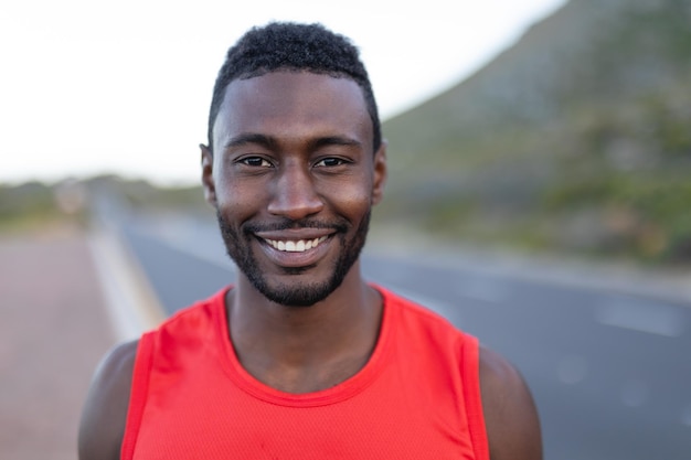 Ritratto di uomo afroamericano in forma in piedi su una strada costiera che guarda l'obbiettivo sorridente. stile di vita sano, esercizio in natura.