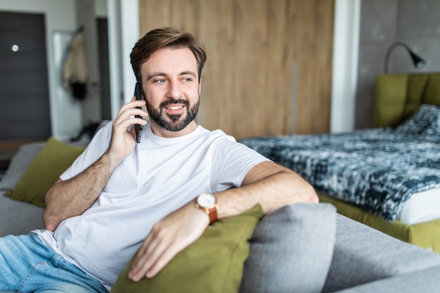 Ritratto di uomo allegro, parlando al telefono, seduto sul divano a casa