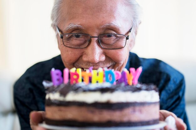 Ritratto di uomo anziano felice che tiene la torta di compleanno al cioccolato con candele colorate