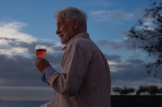 ritratto di uomo anziano seduto di fronte al mare al tramonto con in mano un bicchiere di vino orizzonte sopra