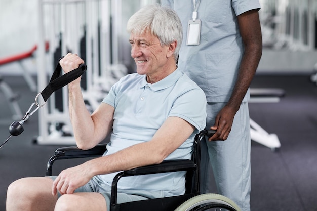 Ritratto di uomo anziano sorridente che usa la sedia a rotelle in palestra durante lo spazio della copia della terapia riabilitativa