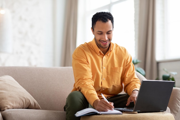 Ritratto di uomo arabo sorridente utilizzando laptop e scrittura