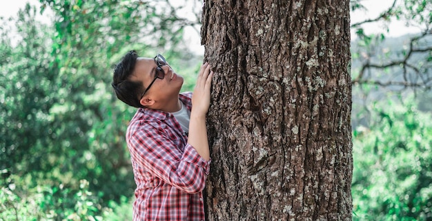 Ritratto di uomo asiatico felice che abbraccia un albero nella foresta Proteggere e amare la natura Concetto di ambiente ed ecologia