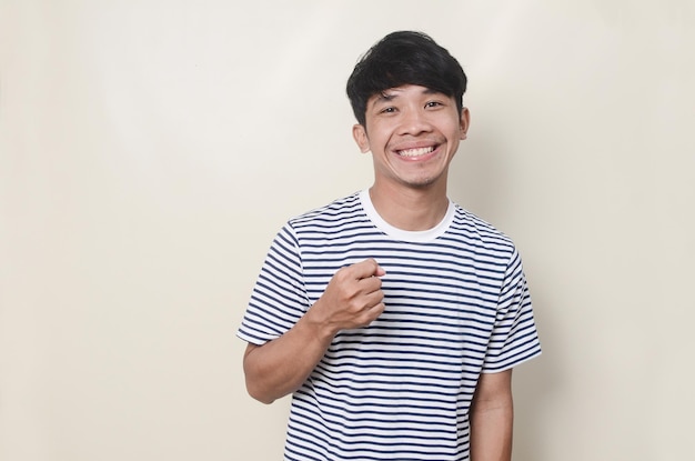 Ritratto di uomo asiatico felice che punta in maglietta a righe su sfondo isolato