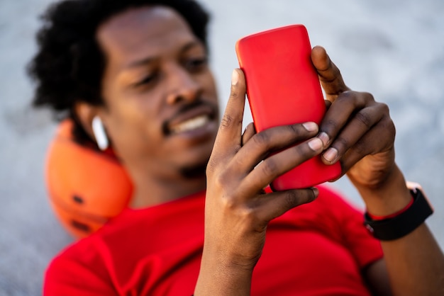 Ritratto di uomo atleta afro utilizzando il suo telefono cellulare mentre posa sul pavimento dopo l'allenamento all'aperto