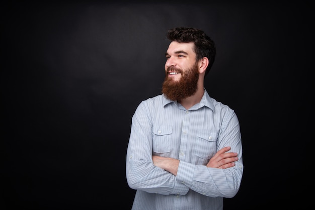 Ritratto di uomo barbuto con le mani incrociate, guardando lontano su sfondo grigio scuro