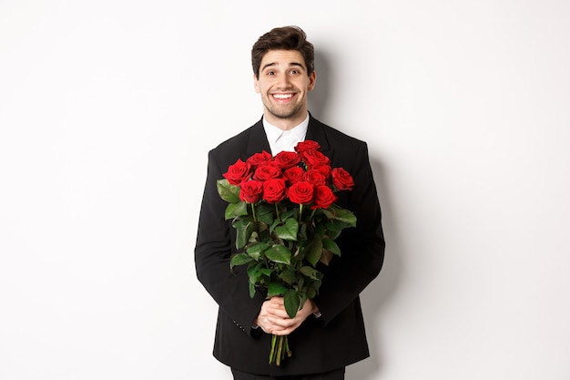 Ritratto di uomo bello in abito nero, tenendo il mazzo di rose e sorridente