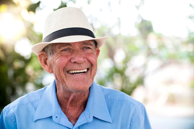 ritratto di uomo brasiliano anziano con cappello bianco guardando un punto nel tramonto e sorridente. Forma orizzontale, copia dello spazio.