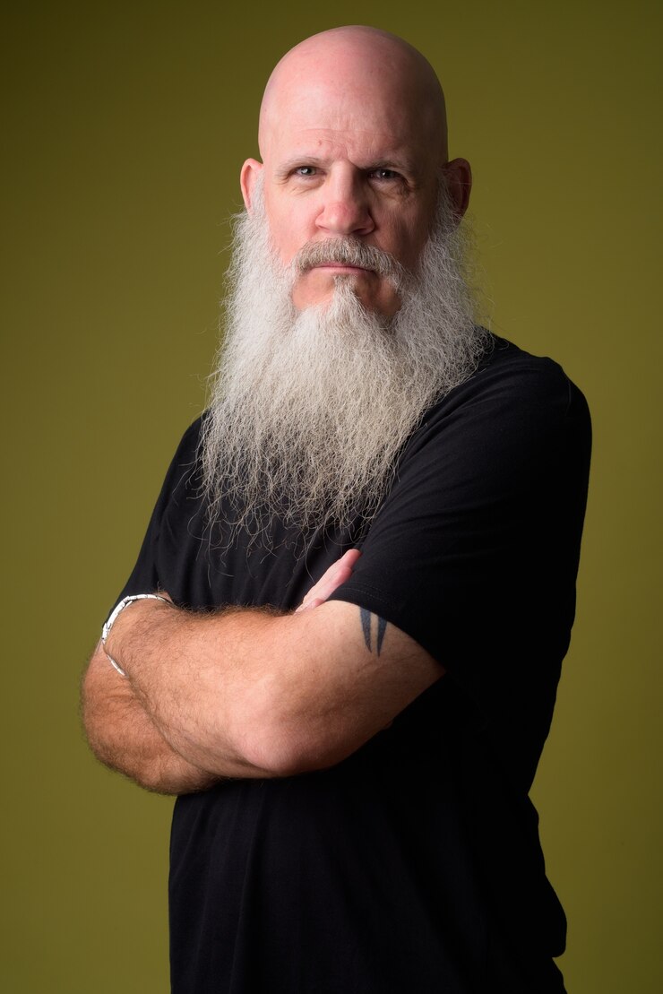 Foto ritratto di uomo calvo maturo con una lunga barba grigia contro la parete colorata