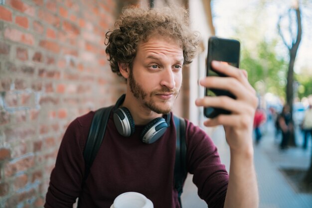 Ritratto di uomo che cattura selfie con il suo telefono mophile all'aperto in strada. Concetto di tecnologia.