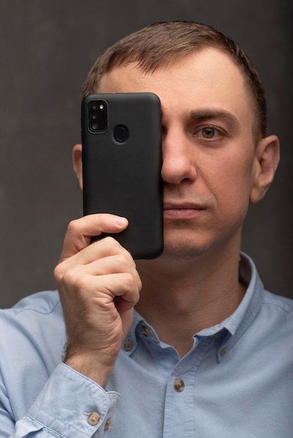 Ritratto di uomo con telefono vicino al viso L'uomo tiene uno smartphone nero Telefono invece della fotocamera concettuale Cornice verticale