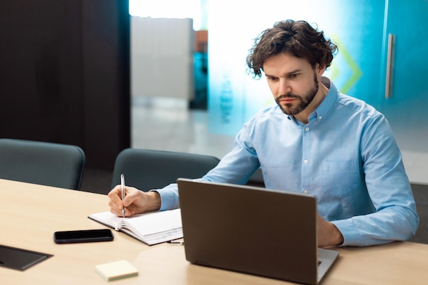 Ritratto di uomo concentrato che utilizza laptop e scrive sul taccuino