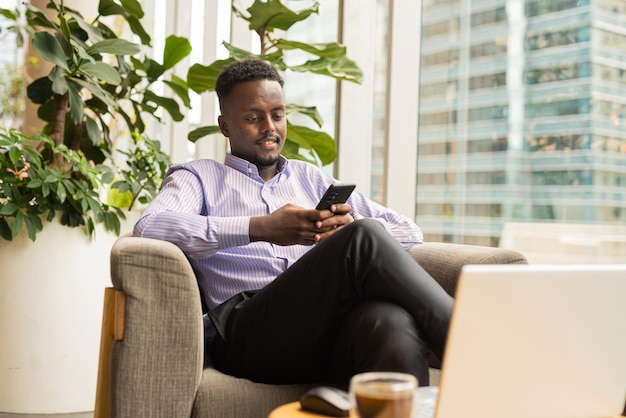 Ritratto di uomo d'affari africano bello seduto nella caffetteria utilizzando il computer portatile