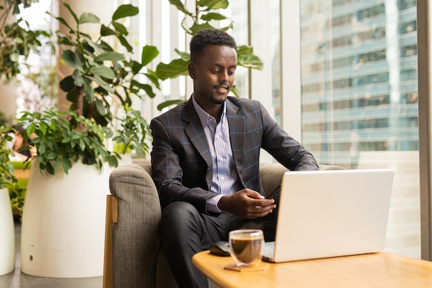 Ritratto di uomo d'affari africano bello seduto nella caffetteria utilizzando il computer portatile