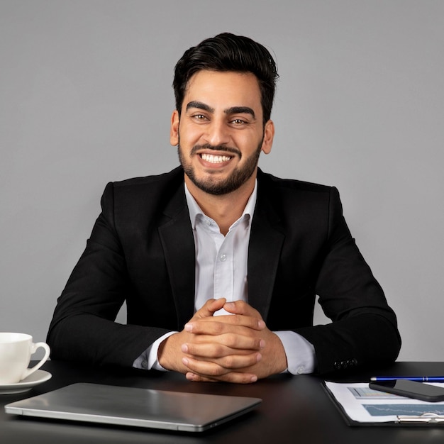 Ritratto di uomo d'affari arabo bello seduto alla scrivania e sorridere alla telecamera