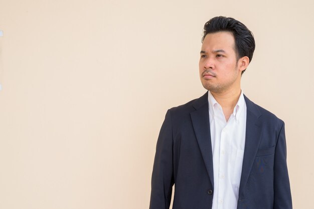 Ritratto di uomo d'affari asiatico che indossa tuta su sfondo semplice mentre pensa
