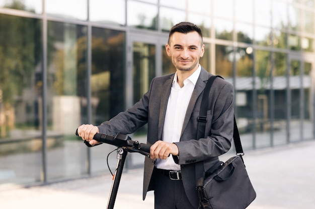 Ritratto di uomo d'affari fiducioso in piedi con scooter elettrico e guardando la tecnologia della fotocamera