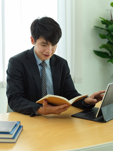 Ritratto di uomo d'affari leggendo le informazioni sul suo libro di pianificazione mentre si lavora con la tavoletta digitale