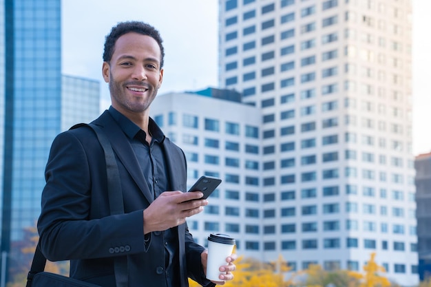 Ritratto di uomo d'affari nero di successo in tuta sorridente guardando gli edifici della fotocamera in background