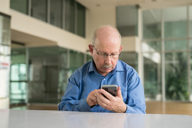 Ritratto di uomo d'affari senior seduto in ufficio e utilizzando il telefono