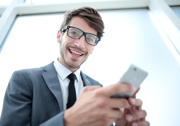 Ritratto di uomo d'affari sorridente che legge il messaggio con lo smartphone in ufficio