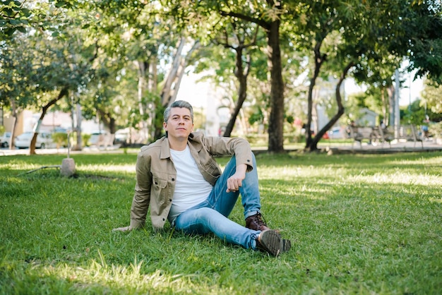 Ritratto di uomo dai capelli grigi in un parco con espressione positiva seduto sull'erba guardando la telecamera