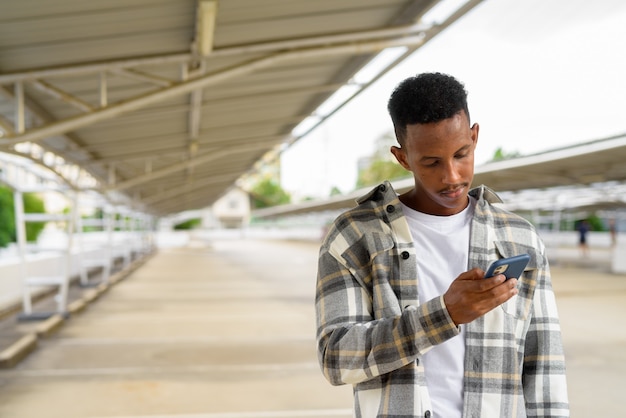 Ritratto di uomo di colore africano all'aperto in città utilizzando il telefono cellulare durante l'estate