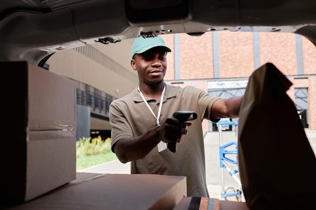 Ritratto di uomo di consegna che scansiona i codici sui pacchi durante lo scarico dello spazio di copia del furgone