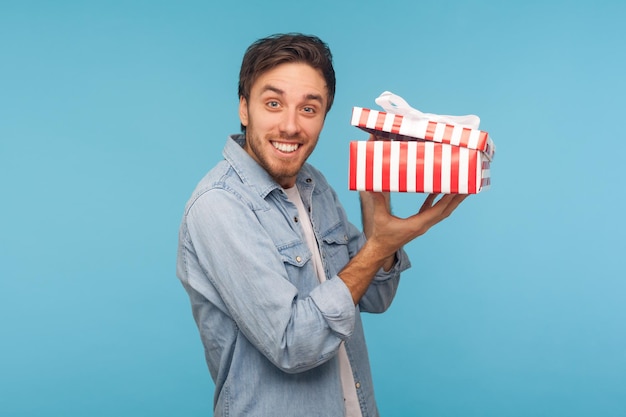 Ritratto di uomo eccitato in camicia di jeans con scatola regalo aperta e guardando la fotocamera con un sorriso gioioso che disimballa il presente soddisfatto con una fantastica sorpresa di compleanno in studio indoor girato isolato