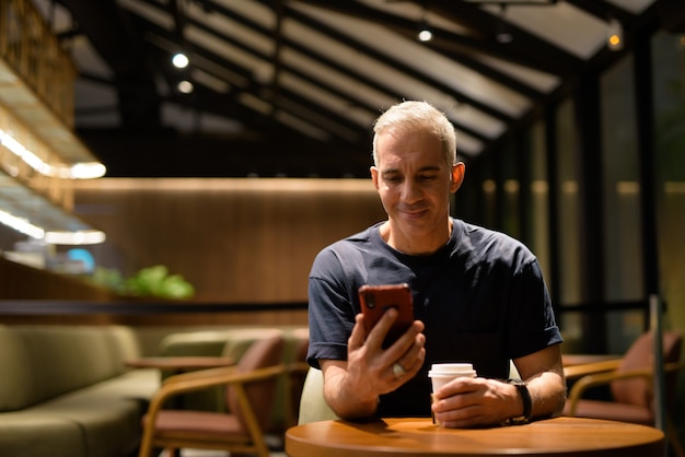 Ritratto di uomo felice all'interno della caffetteria di notte utilizzando il telefono cellulare, ripresa orizzontale