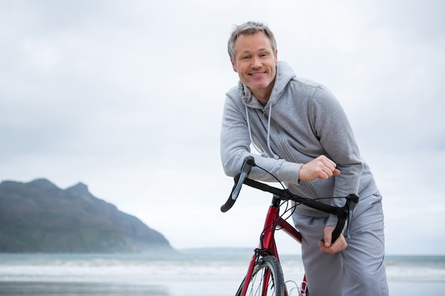 Ritratto di uomo felice appoggiato sulla bicicletta in spiaggia